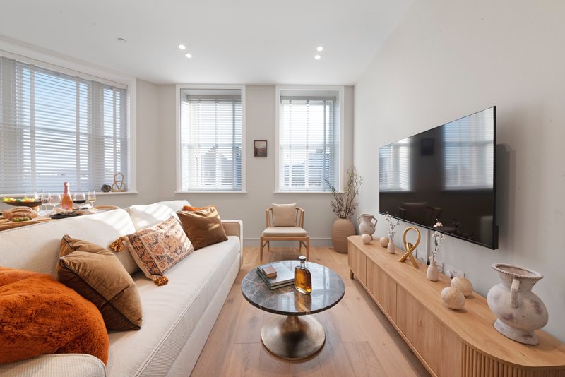 Modern studio bedroom with bed, TV, windows, and sitting area with chairs
