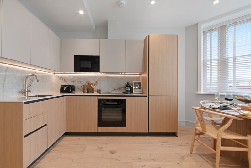 Modern kitchen with light wood and white cabinetry, stainless steel fridge, dining table and chairs