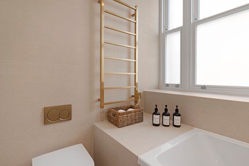Modern bathroom with toilet, sink, window, wooden ladder and toiletry bottles on counter