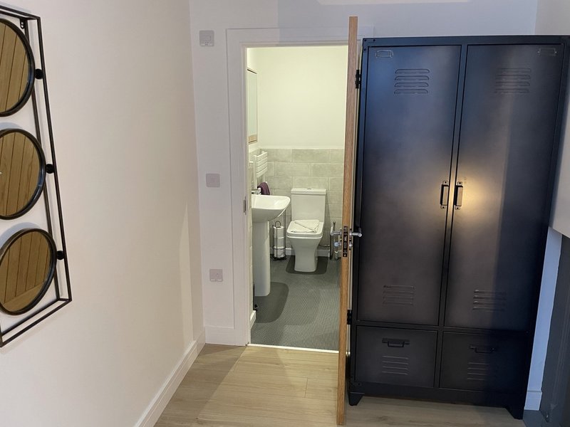 Hallway with wooden flooring, dark metal wardrobe, and open bathroom door showing toilet and sink