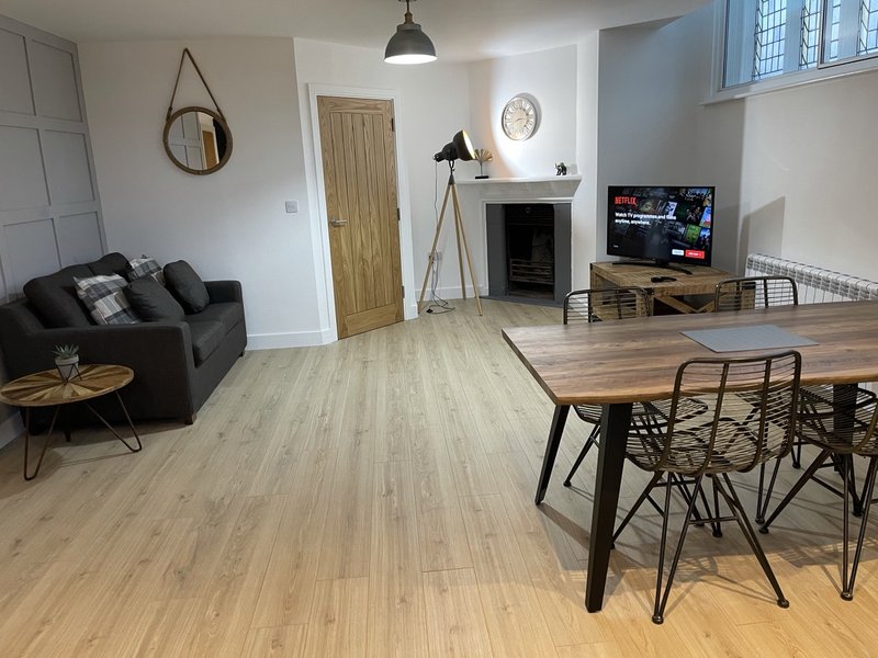 Open-plan living area with black sofa, wooden dining table, fireplace and TV entertainment setup
