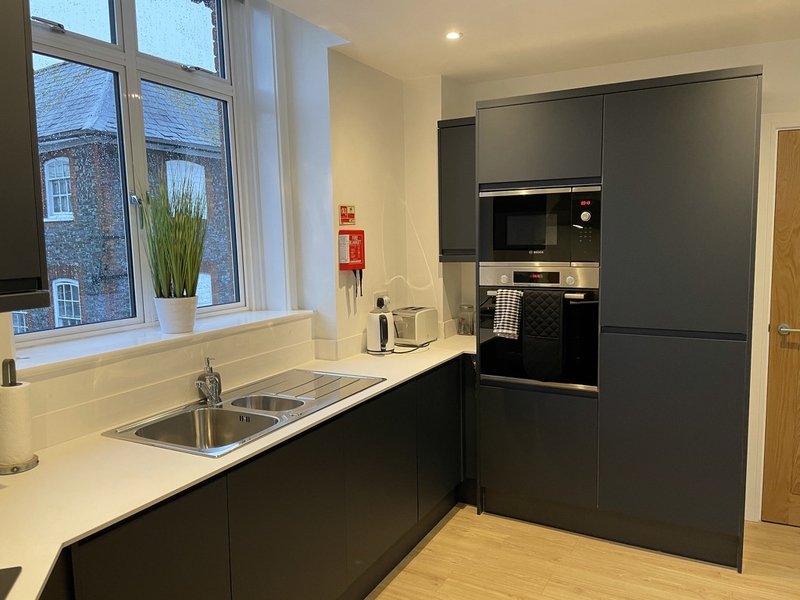 Modern kitchen with black cabinetry, white countertop, sink, and large window overlooking street