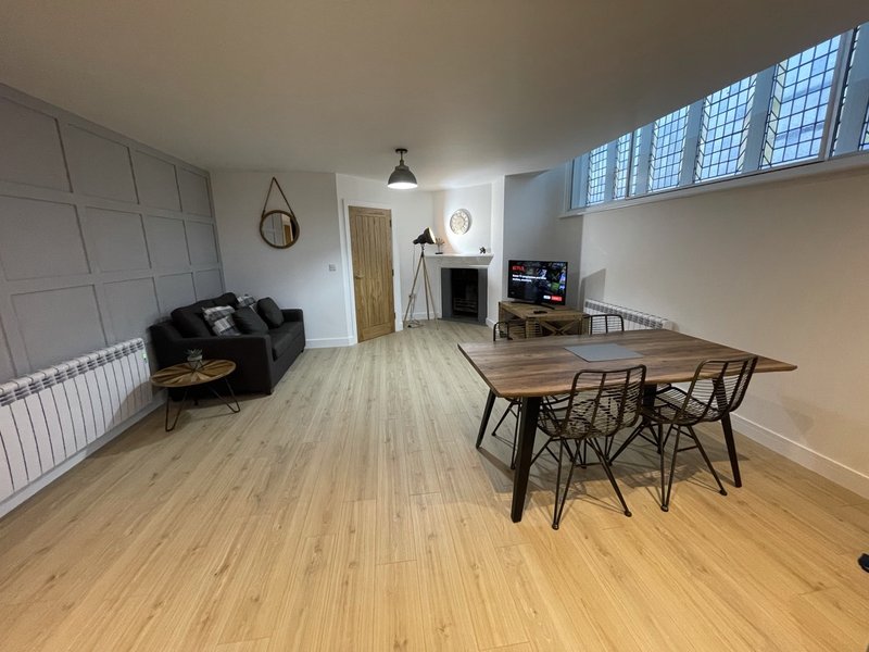 Open-plan living space with wooden flooring, dining table, black sofa, and fireplace