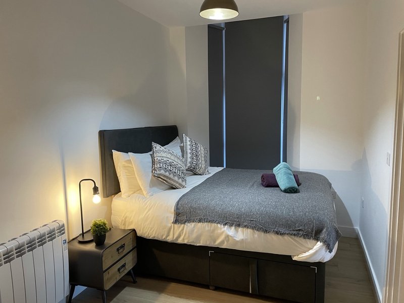 Bedroom with double bed, black headboard, bedside lamp, grey throw blanket and decorative pillows