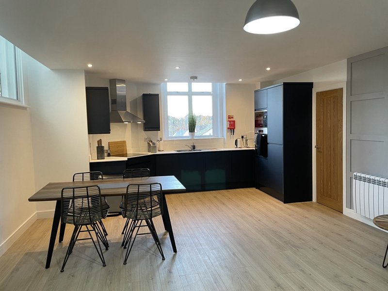 Modern open-plan kitchen and dining area with black cabinetry, dining table, and wooden flooring