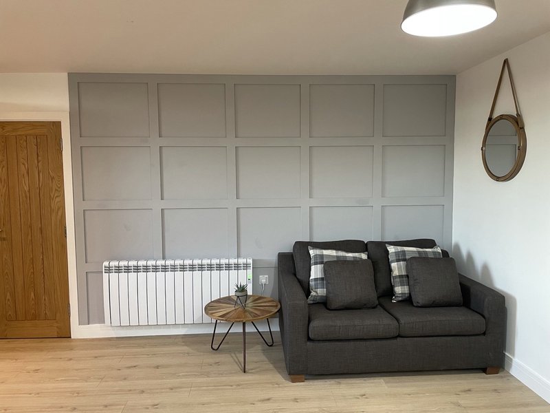 Living room with gray sofa, small wooden side table, radiator, and wall-mounted mirror