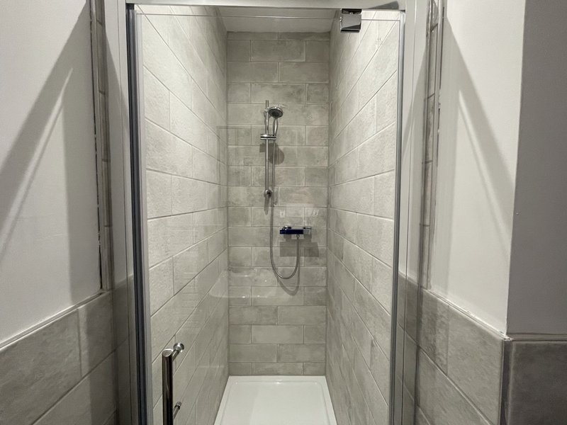 Modern shower enclosure with gray tile walls, glass door and rainfall showerhead