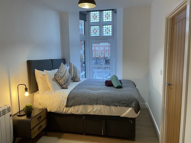 Modern bedroom with single bed, yellow bedding, cushions, pendant light and street view window