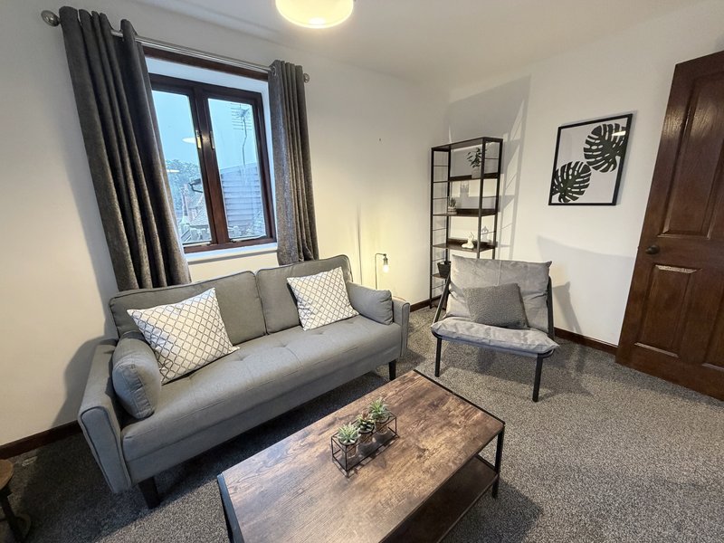 Modern living room with grey sofa, armchair, wooden coffee table and window with curtains