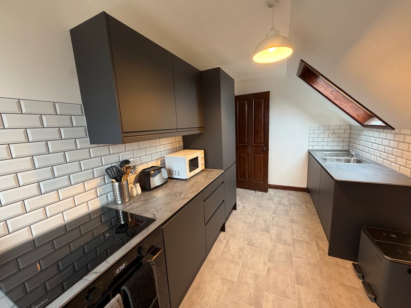 Modern galley kitchen with dark cabinetry, subway tile backsplash, pendant light and wooden flooring