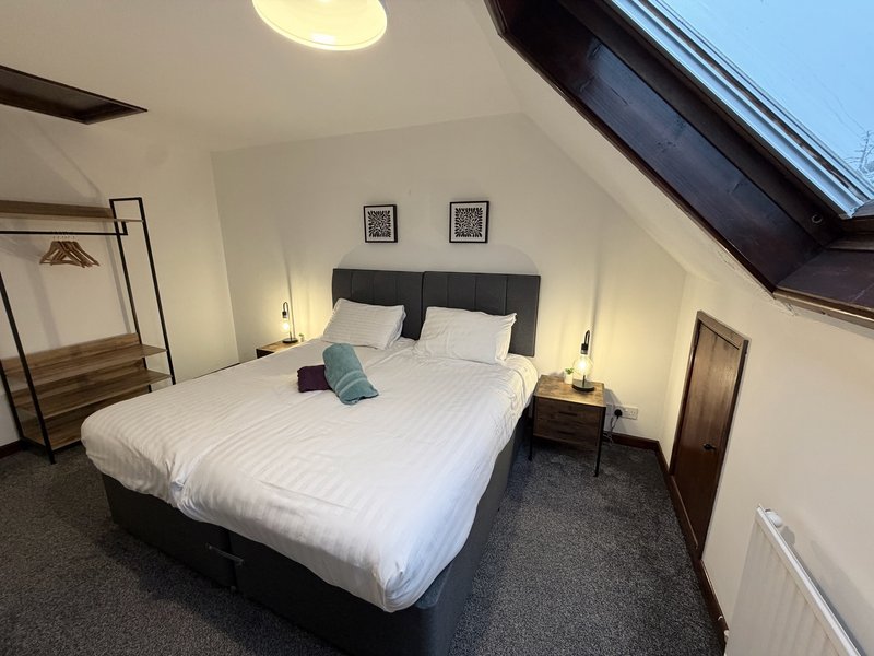 Attic bedroom with double bed, black headboard, white bedding, teal cushion, skylights