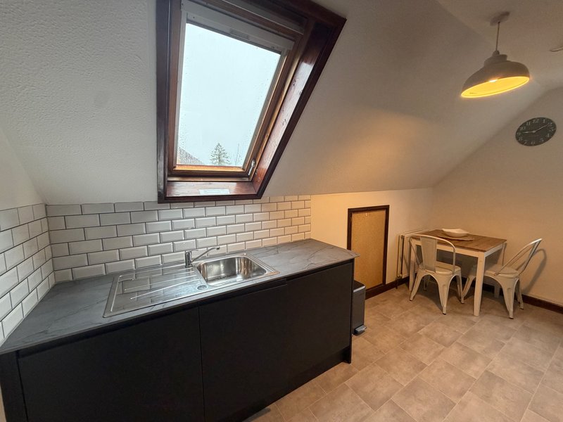 Attic kitchen with skylight, sink, black cabinetry, subway tile backsplash, and wooden dining chairs