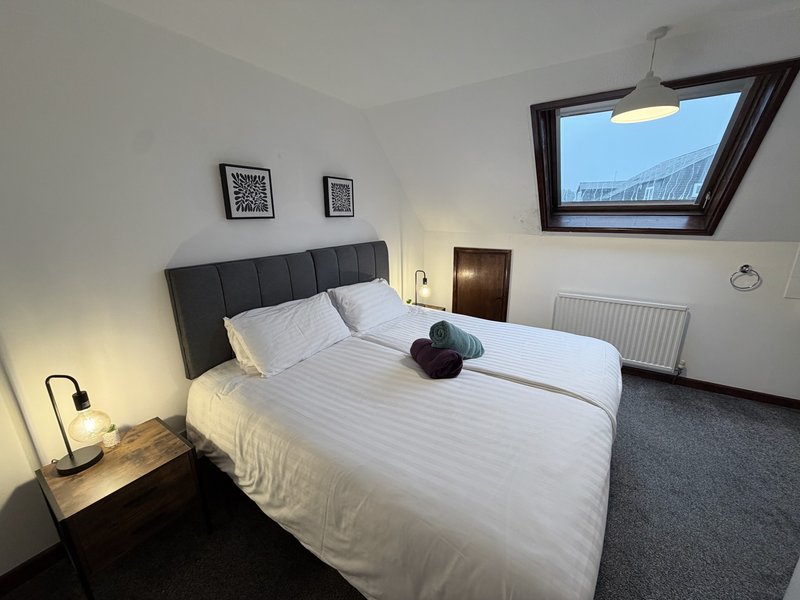 Modern bedroom with double bed, black headboard, bedside lamp, skylight window and radiator