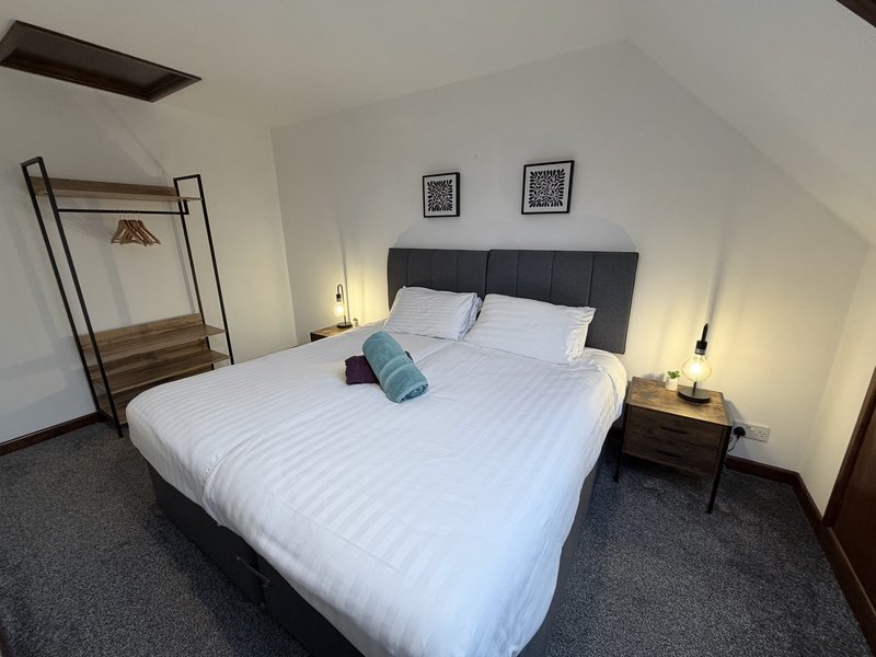 Modern bedroom with double bed, dark headboard, bedside tables, and clothing rack