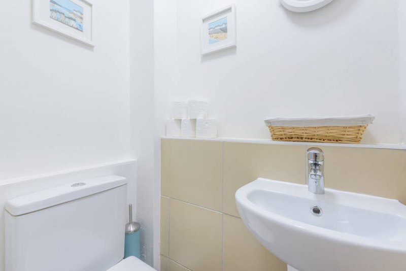Clean bathroom with white sink, toilet, beige tiling and wall-mounted accessories