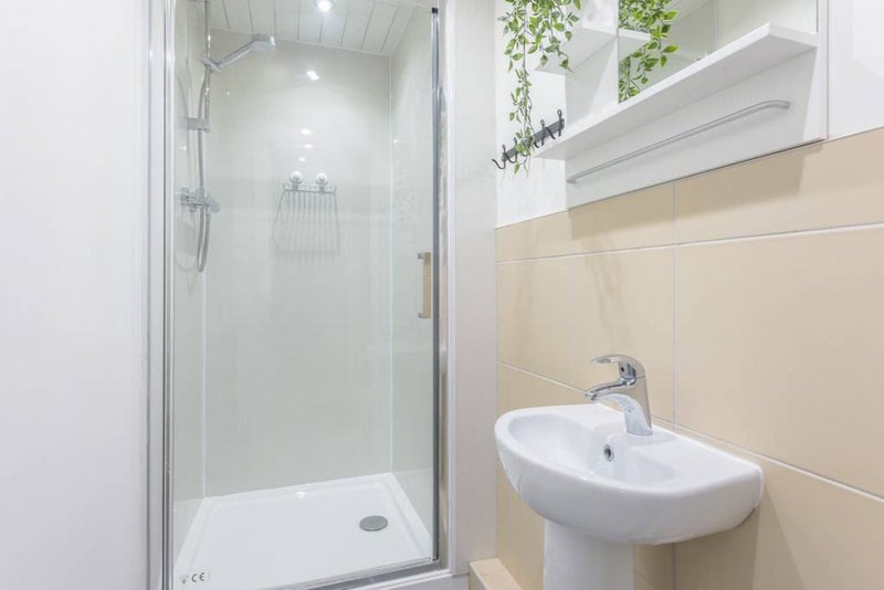 Modern bathroom with shower enclosure, white sink, and beige tile walls