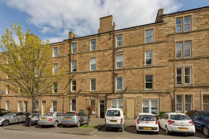 Sandstone tenement building with parked cars on street and leafy tree in front