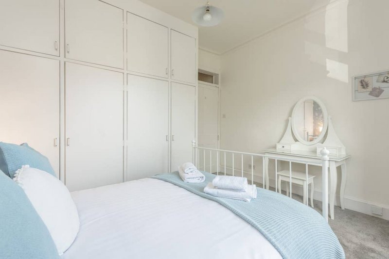 Bright bedroom with double bed, white built-in wardrobes, dressing table and oval mirror