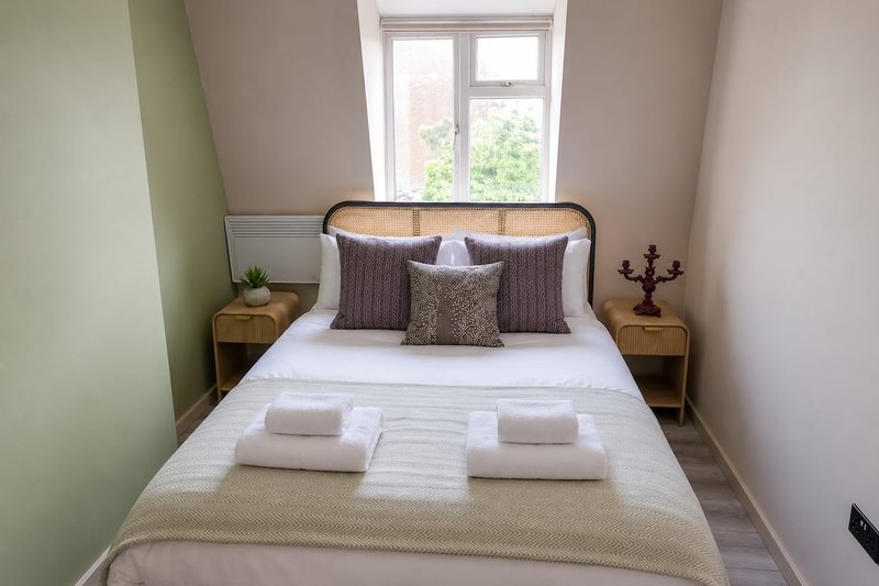 Compact bedroom with double bed, woven headboard, bedside tables and window with garden view