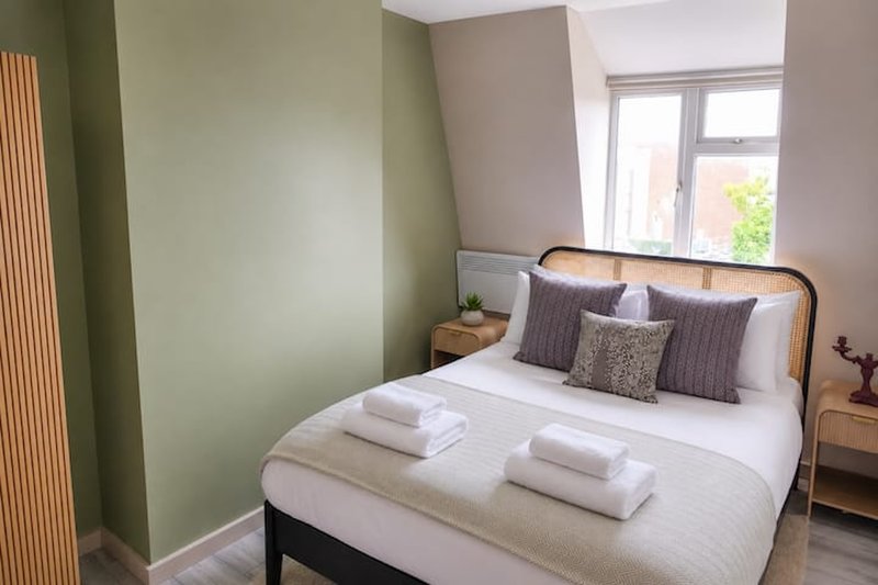 Bright bedroom with double bed, rattan headboard, green accent wall and window