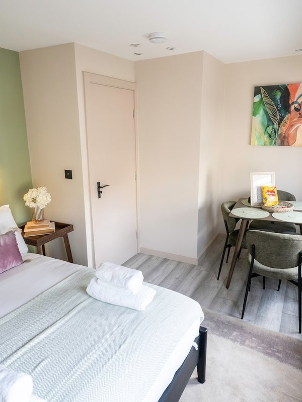 Bedroom with double bed, desk area, chair, and white door against pale walls