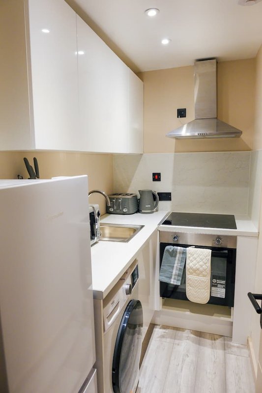 Compact modern kitchen with white cabinetry, integrated appliances, and wood-effect flooring