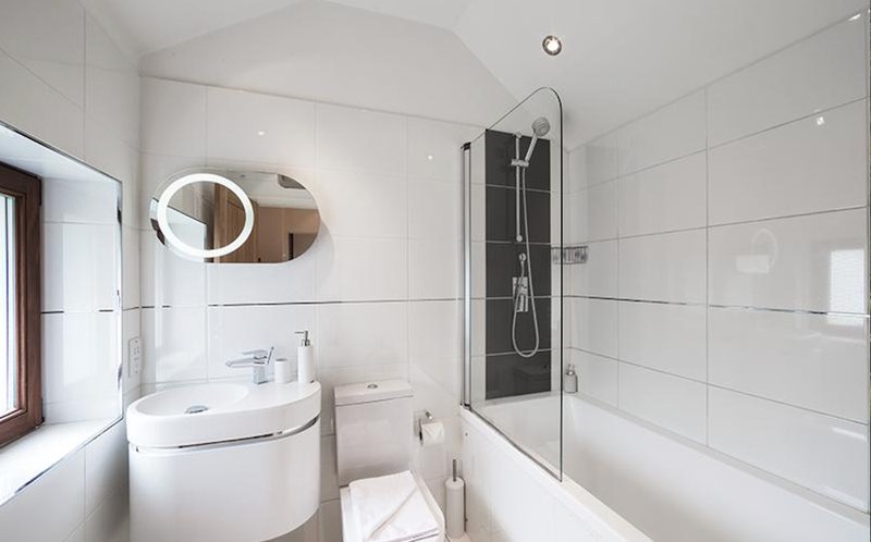 Modern bathroom with white tiles, corner sink, illuminated mirror, shower enclosure and toilet