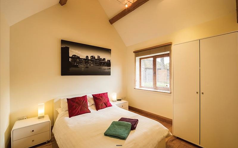 Bedroom with double bed, red cushions, bedside lamps, built-in wardrobe and cityscape artwork