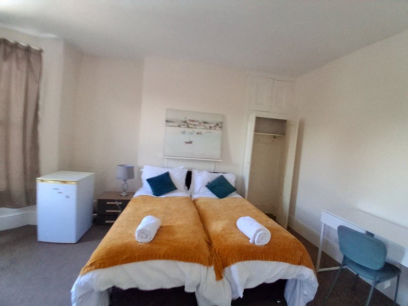 Bedroom with twin beds, orange bedding, blue cushions, white bin, and coastal artwork
