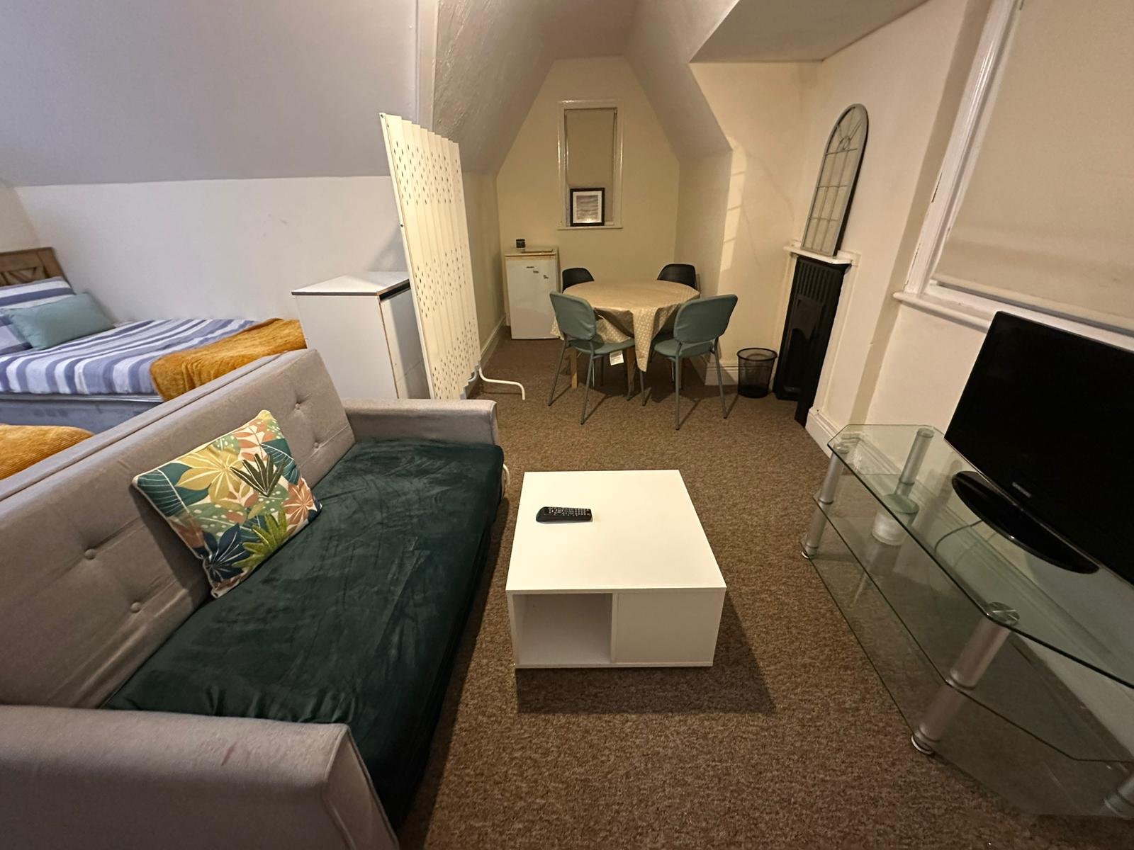 Open-plan attic bedroom-lounge with sofa, bed, dining table and TV