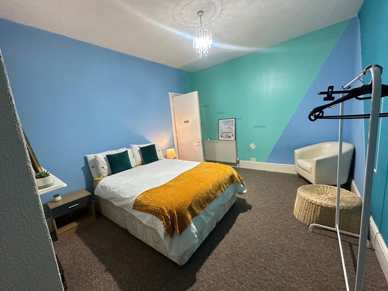 Colorful bedroom with blue and turquoise walls, white bed, yellow throw, and modern furnishings