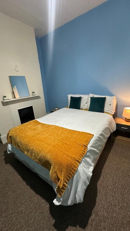 Bedroom with double bed, yellow throw, blue accent wall, mirror and bedside lamps