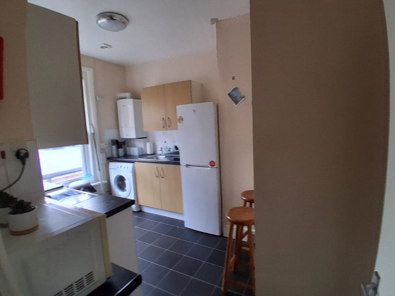 Compact kitchen with white fridge, washing machine, cooker and wooden dining chairs