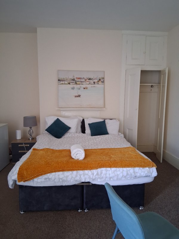 Bedroom with double bed, orange throw, blue cushions, bedside lamp and framed artwork