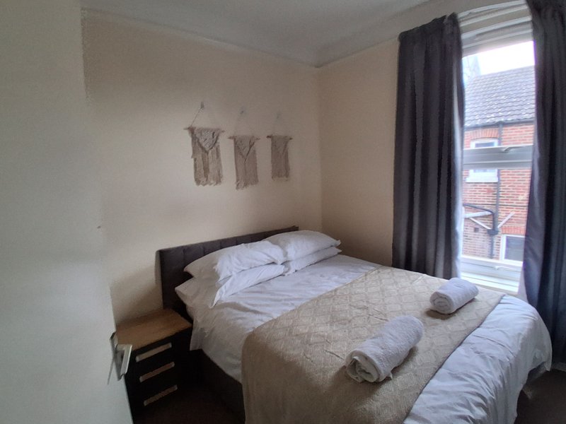 Bedroom with double bed, dark wooden frame, white bedding, dark curtains and window view
