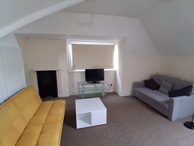 Bright attic living room with yellow sofa, gray couch, TV stand and white coffee table
