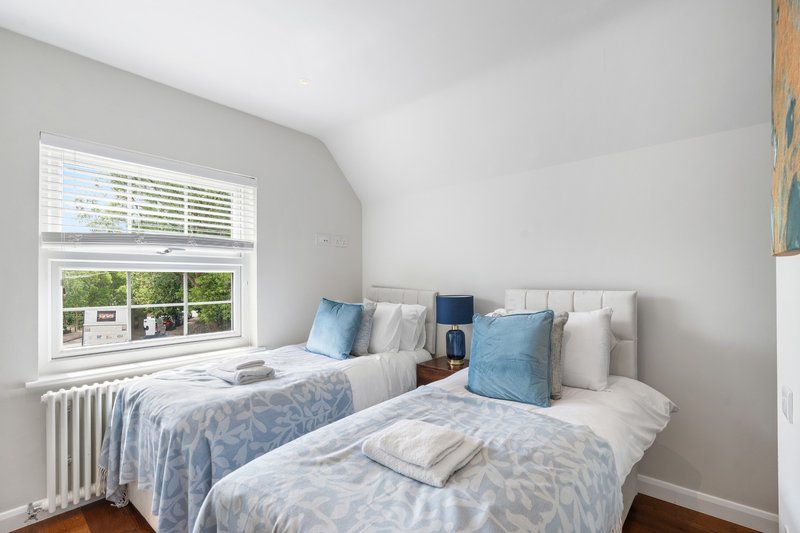 Bright bedroom with two single beds, blue patterned bedding, cushions, and large window overlooking garden