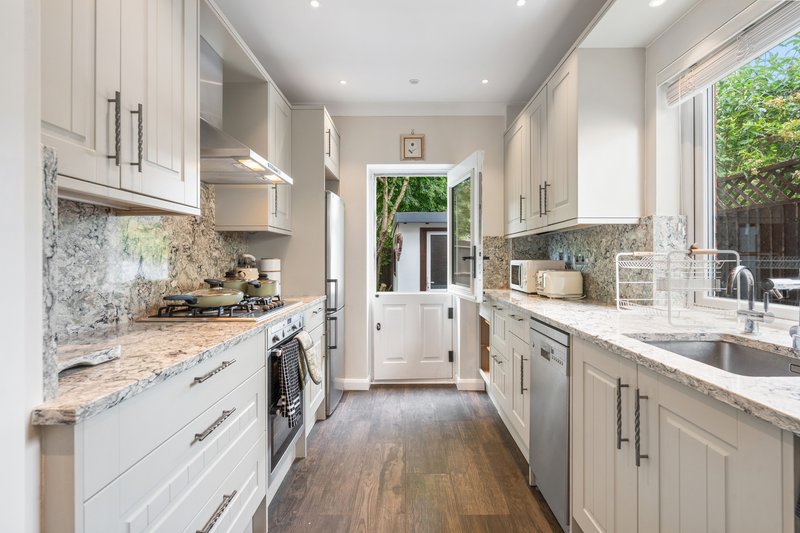 Modern galley kitchen with white cabinetry, marble countertops, stainless steel appliances and garden view