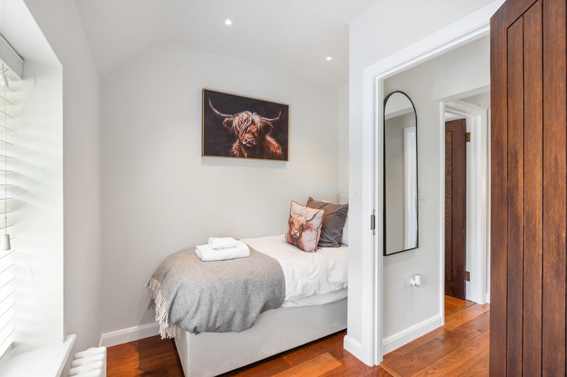 Small bedroom with single bed, grey bedding, framed animal artwork, and wooden flooring
