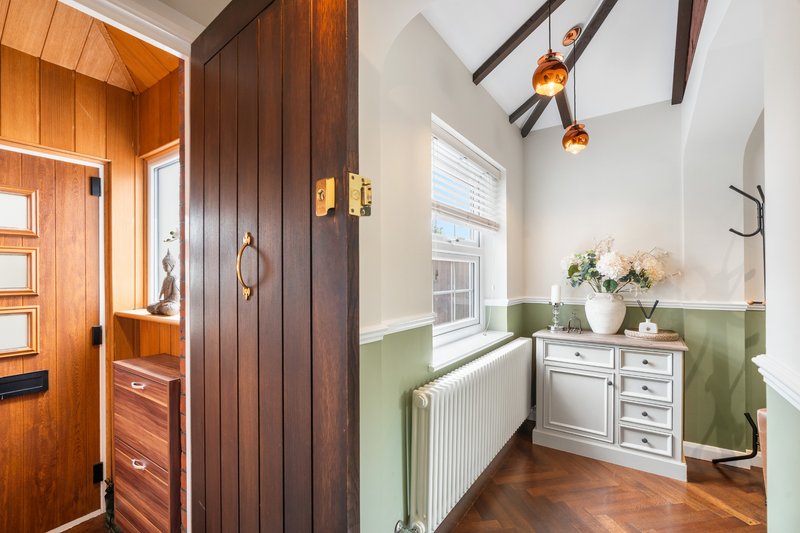 Bright hallway with wooden doors, green and white wall panelling, radiator and small dresser with flowers