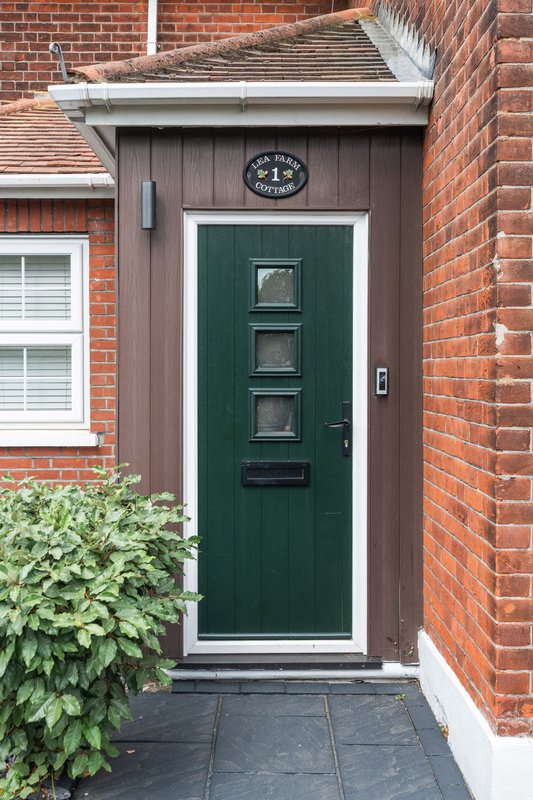Brick house entrance with green door, brown porch, and climbing ivy plant