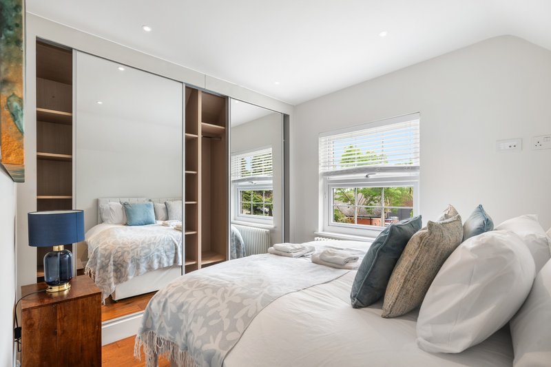 Bright bedroom with two beds, large mirror, wooden furniture and garden views