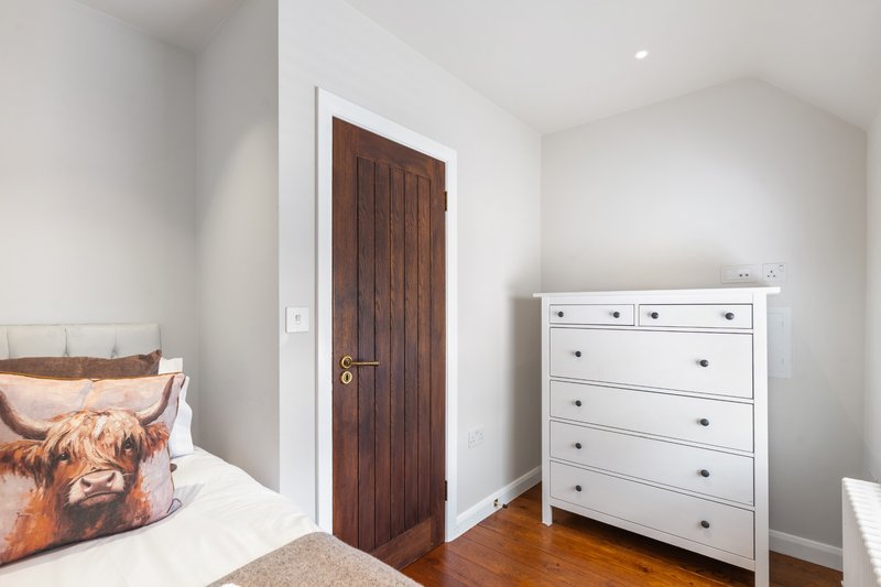 Bedroom with single bed, white dresser, wooden door and hardwood flooring