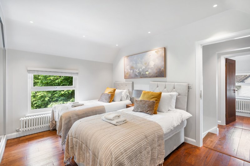 Bright bedroom with two single beds, wooden floor, large window and framed artwork