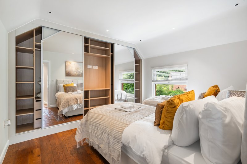 Bright bedroom with double bed, yellow cushions, mirrored wardrobe and wooden flooring