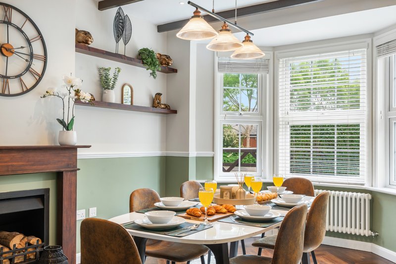 Dining room with set table, fireplace, wall shelves, pendant lights and garden view