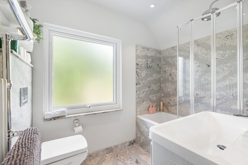 Modern bathroom with white toilet, freestanding bathtub, glass shower enclosure, and window