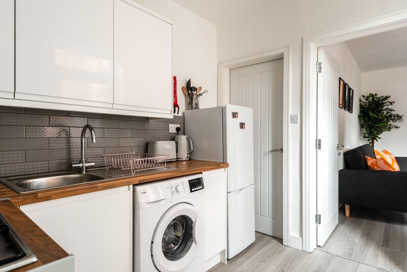 Modern kitchen with white cabinets, wooden countertop, washing machine, and gray tile backsplash