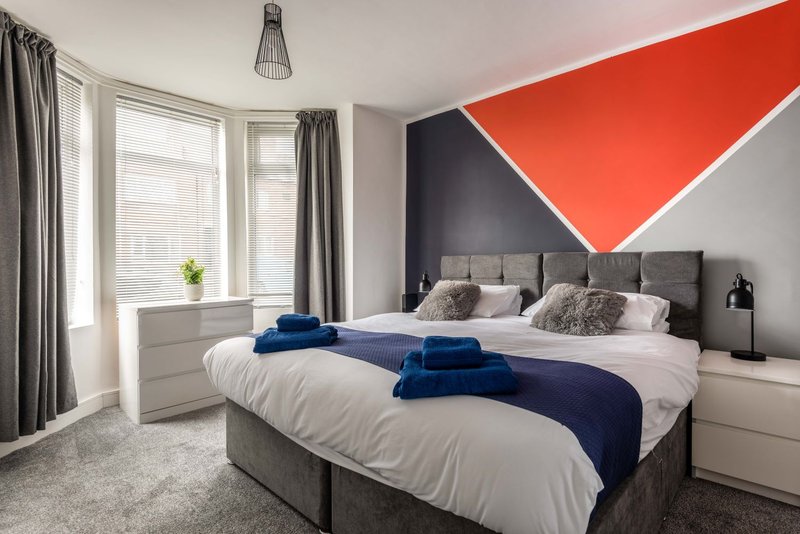 Modern bedroom with twin beds, geometric wall art, large windows and grey curtains