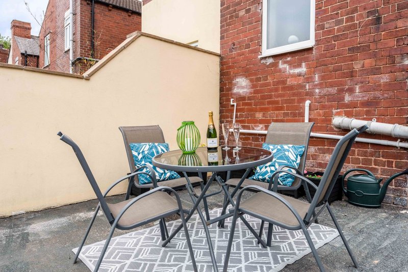 Outdoor patio seating area with table, chairs, wine bottle, and potted cactus against brick wall